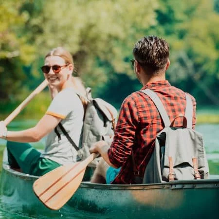Couple adventurous explorer friends are canoeing in a wild river surrounded by the beautiful nature.
