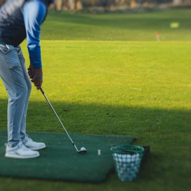 Group of golfers practicing and training golf swing on driving range practice, men playing on golf course, golf ball at golfing complex club resort, summer sunny day