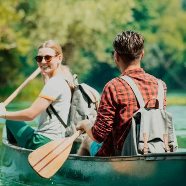 Couple adventurous explorer friends are canoeing in a wild river surrounded by the beautiful nature.