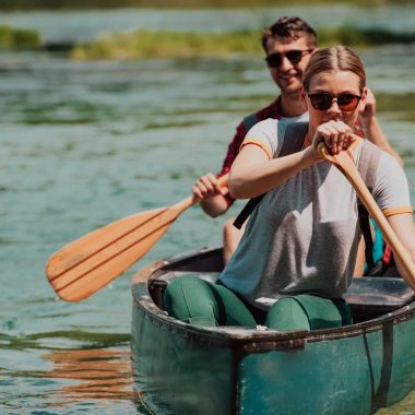 Couple adventurous explorer friends are canoeing in a wild river surrounded by the beautiful nature.